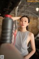 A woman in a gray tank top leaning against a car.