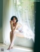 A woman sitting on a window sill in a white dress.