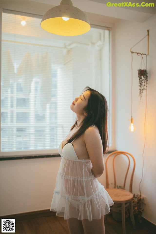 A woman in a white dress standing in front of a window.