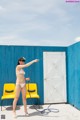 A woman in a bikini holding a hose in front of a blue wall.