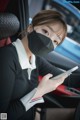 A woman wearing a face mask while sitting in a car looking at her phone.