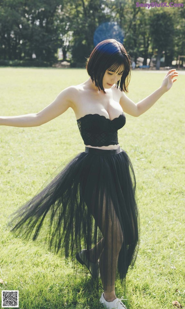 A woman in a black dress is dancing in the grass.