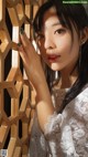 A woman in a white dress leaning against a wooden wall.