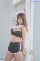 A woman in a black bra and black shorts leaning against a window.