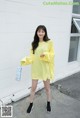 a woman standing in front of a white wall wearing a yellow dress