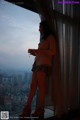 A woman standing in front of a window looking out at the city.